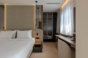 a bedroom with a white bed and a desk and window at Nesean Plaza Hotel in Heraklio