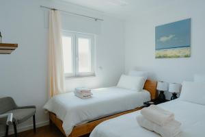 a bedroom with two beds and a chair and a window at Kalumi Aparthotels - Japandi-Style Apartments with Terrace, Pergola, and Portuguese BBQ in Vila Nova de Milfontes