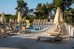 a group of chairs and umbrellas next to a pool at Family Hotel Adria - All inclusive in Biograd na Moru