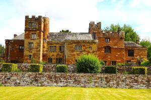 an old castle with a stone wall and a grass field at Dalston Hall in Carlisle