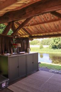 an outdoor kitchen under a wooden roof with a river at Glempingosta in Bauska
