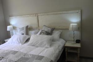 a bed with white sheets and pillows and two lamps at The Alchemist's Place in Oudtshoorn
