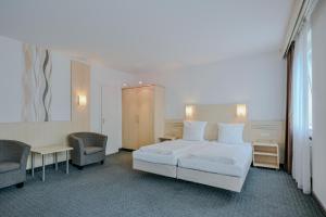 a hotel room with a bed and two chairs at Hotel Mondial Comfort - Frankfurt City Centre in Frankfurt