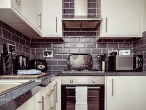a kitchen with white cabinets and a purple tiled wall at Chalet 4 in Flookburgh