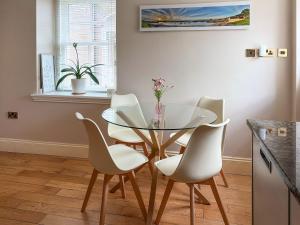 a dining room with a glass table and white chairs at 2 The Langhouse in Inverkip