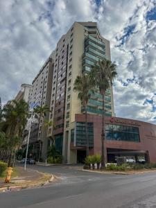 a large building with palm trees in front of it at Lindo Flat Part Grand Mercure Varanda aconchegante in Brasília