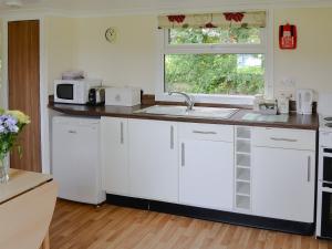 a kitchen with white cabinets and a sink and a window at White Moth - Uk12697 in Stalham