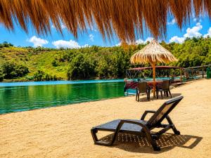 a beach with a table and chairs and a straw umbrella at Hotel Pietrasanta Cabañas frente a la Represa Peñol Guatape in Guatapé