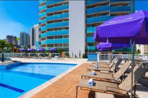 a pool with chairs and umbrellas next to a building at Flat Mercure Nova Iguaçu in Nova Iguaçu