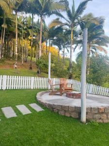 a park with two benches and a fence and palm trees at Chalé do amor, sítio pousada vô Maneca in Timbó