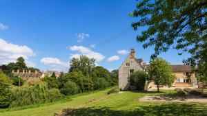 an old house on a grassy field with a castle in the background at Almsbury Farmhouse in Winchcombe