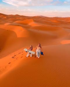 two people in the desert with their surfboards at Sahara Nomadic Luxury Camp in Merzouga