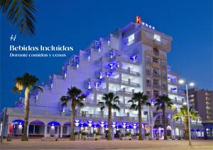 ein großes weißes Gebäude mit Palmen davor in der Unterkunft Hotel Los Delfines in La Manga del Mar Menor