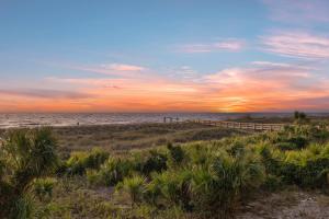 a beach with a fence and the ocean at sunset at The Gardens 703 in Tybee Island