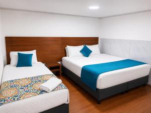 a bedroom with two beds with blue and white pillows at Hotel Casa Lamay in Bogotá