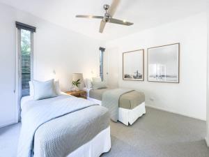 a white bedroom with two beds and a ceiling fan at Stunning Views, Private Pool Near Hastings St in Noosa Heads