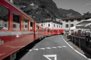 two red trains parked on a street next to buildings at Dimora Perla di Villa - Spacious Wine Estate Retreat near Bernina Express in Villa di Tirano