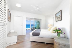 a white bedroom with a bed and a vase of flowers at Ocean Panorama With Private Pool! in Noosa Heads +10 photos