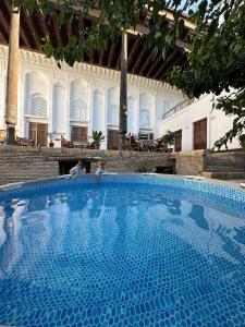two people sitting next to a large blue swimming pool at Merik Boutique in Bukhara