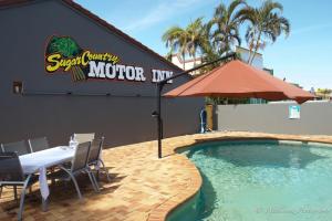 un restaurante con mesa y sombrilla junto a una piscina en Sugar Country Motor Inn, en Bundaberg