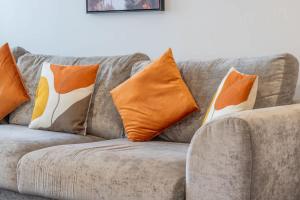 a gray couch with orange and white pillows on it at Park View-modern 2 bed apartment in Motherwell