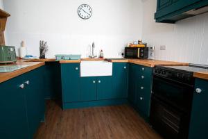 a kitchen with blue cabinets and a clock on the wall at Castle Grant - 4 Bed Cottage in Gardenstown in Gardenstown +28 photos
