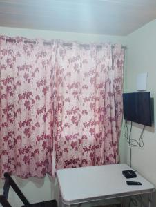 a room with a pink curtain with a desk and a television at Garcia Suite 2 in Blumenau