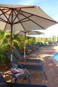 - un groupe de chaises longues et de parasols à côté de la piscine dans l'établissement Exmouth Escape Resort, à Exmouth