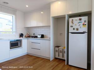 a kitchen with white cabinets and a white refrigerator at Waterview Spacious Bliss - 2 Beds in Porirua +8 photos