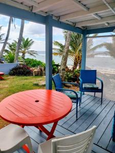 a red table and chairs on a deck with the beach at Heron's Reef Beach Shack Matavera in Matavera