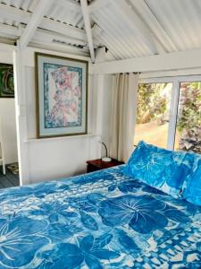 a bedroom with a bed with blue sheets and a window at Heron's Reef Beach Shack Matavera in Matavera