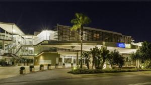 a large building with a palm tree in front of it at Bugalmaa - Cotton Beach in Casuarina