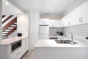 a white kitchen with a sink and a refrigerator at Moondarah: Pet-Friendly Escape in Noosa Heads