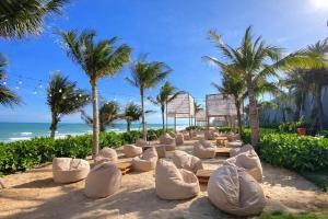 a beach with white chairs and palm trees at Mandala Pearl Resort in Phan Thiet