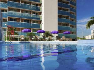 a swimming pool with purple umbrellas and chairs and a building at Mercure Rio de Janeiro Nova Iguaçu in Nova Iguaçu