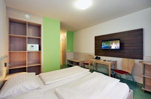 a room with two beds and a desk and a tv at Hotel Kolping Wien Zentral in Vienna