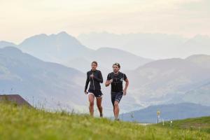 two people walking on a hill with mountains in the background at Das Hohe Salve Sportresort, 4 Sterne Superior in Hopfgarten im Brixental