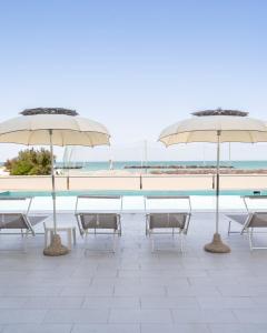 two tables and chairs with umbrellas next to a beach at Hotel Embassy in Pesaro