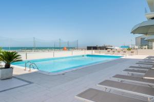 a swimming pool with chairs and the ocean in the background at Hotel Embassy in Pesaro