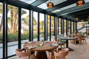 a restaurant with tables and chairs and large windows at Kimpton Aysla Mallorca by IHG in Santa Ponsa