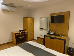a bedroom with a bed and a desk and a television at The Hermitage by The Cosy Hotels Near Lotus Temple in New Delhi