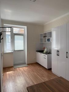 an empty kitchen with white cabinets and a door at Yhome in Karakol
