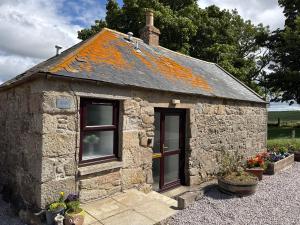 a small stone building with windows and flowers at Altons Bothy Guest House in Kinmuck