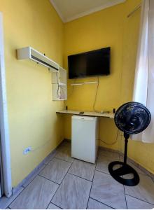 a room with a tv on a yellow wall with a chair at Pousada Nova Onda in Paranaguá