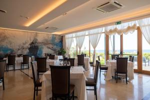 a restaurant with white tables and chairs and windows at Hotel Scoglio Degli Achei in Torre Santa Sabina