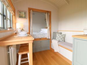 a small room with a bed and a desk with a mirror at Meadow Shepherds Hut in Ashbourne