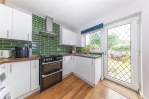 a kitchen with white cabinets and a green brick wall at Entire 3 bedroom house in Luton