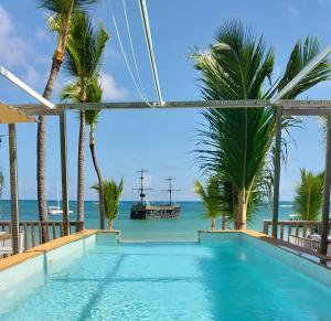 a swimming pool with palm trees and a boat in the water at Hotel Bloom Garden Beach Punta Cana in Punta Cana