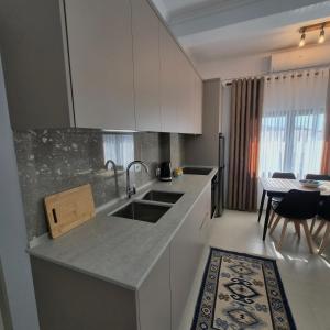 a kitchen with white cabinets and a sink and a table at Kypsel Apartment in Durrës