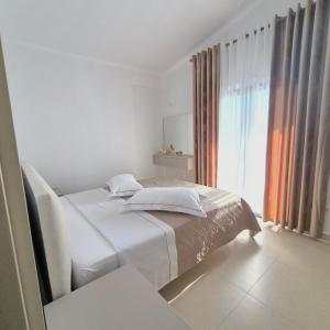 a white bedroom with a bed and a large window at Kypsel Apartment in Durrës